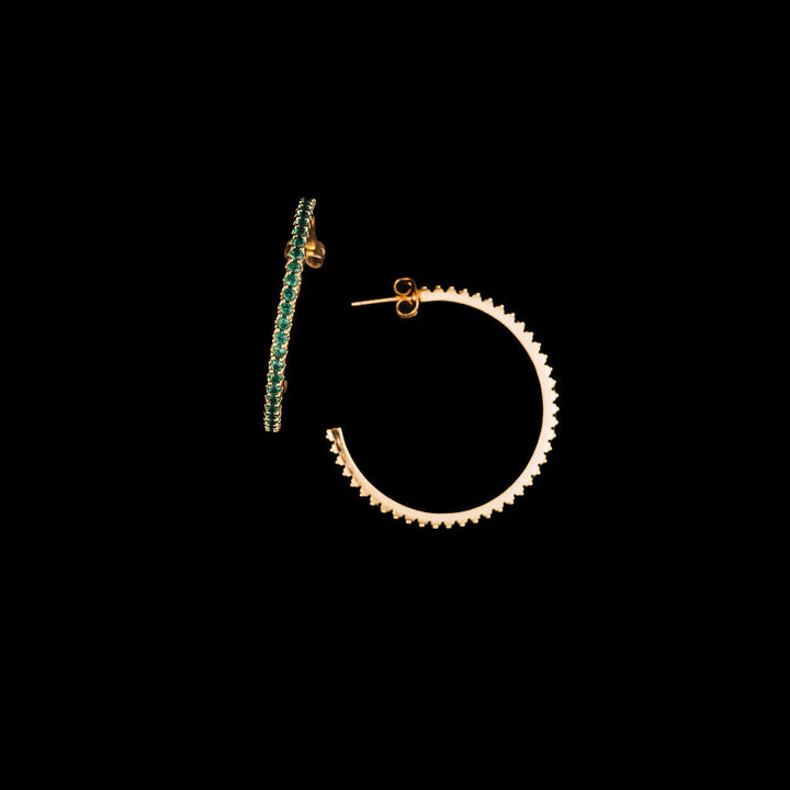 Gold hoop earring with green gemstones on a black background