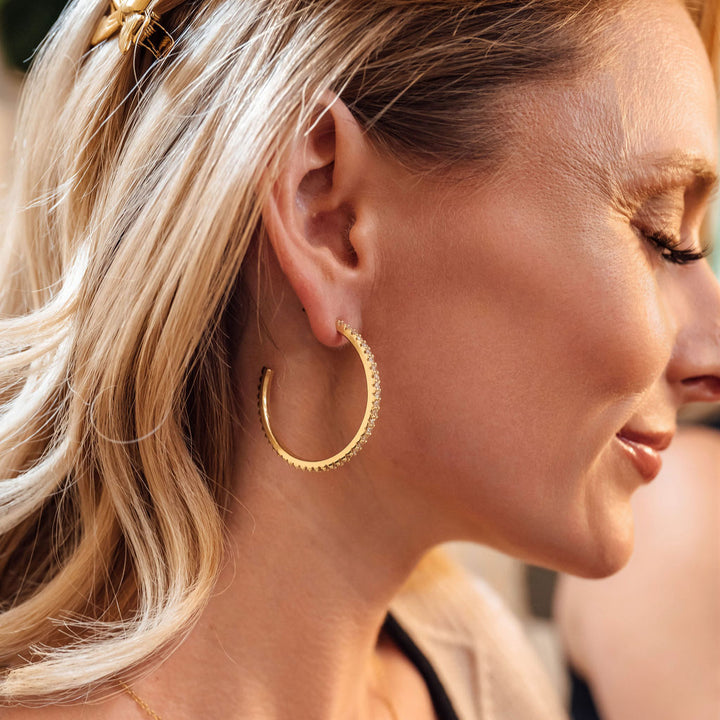 Close-up of a woman wearing gold hoop earrings and a necklace.