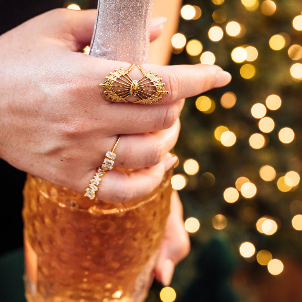 Hand holding a bottle of champagne with gold rings with a blurred festive background