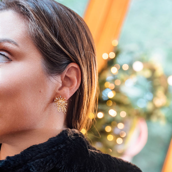 Close-up of a woman wearing gold earrings with a blurred festive background