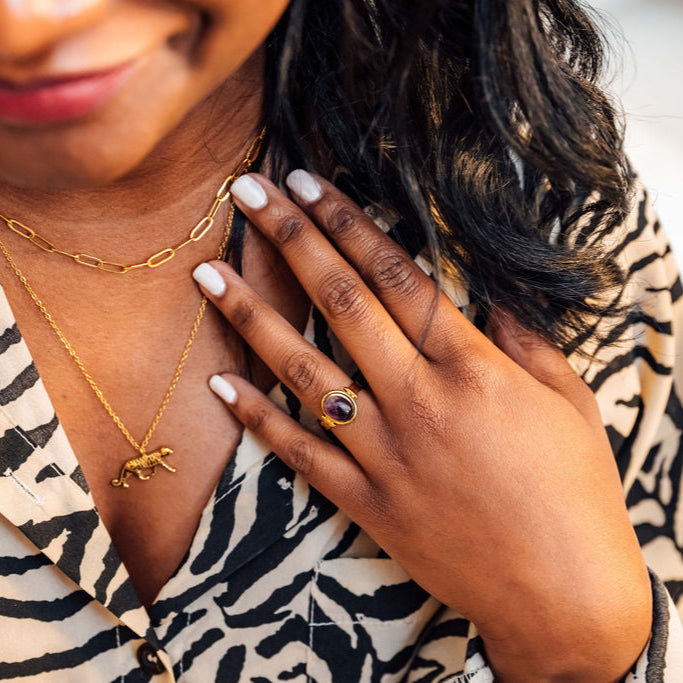 Woman wearing gold  tiger necklaces and an amethyst ring, with a blurred background
