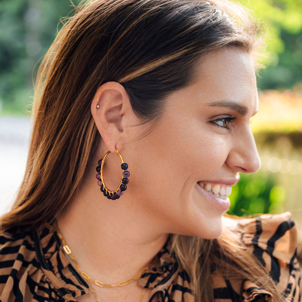 Woman wearing amethyst hoop earrings and a tiger-striped blouse with a blurred outdoor background