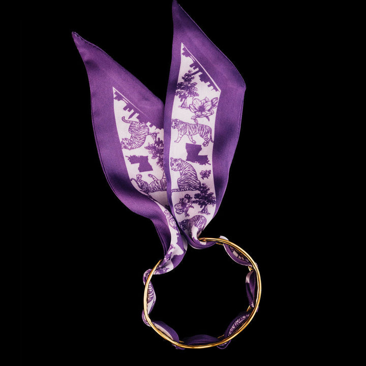 Gold cuff bracelets with purple scarf woven through it  on a black background