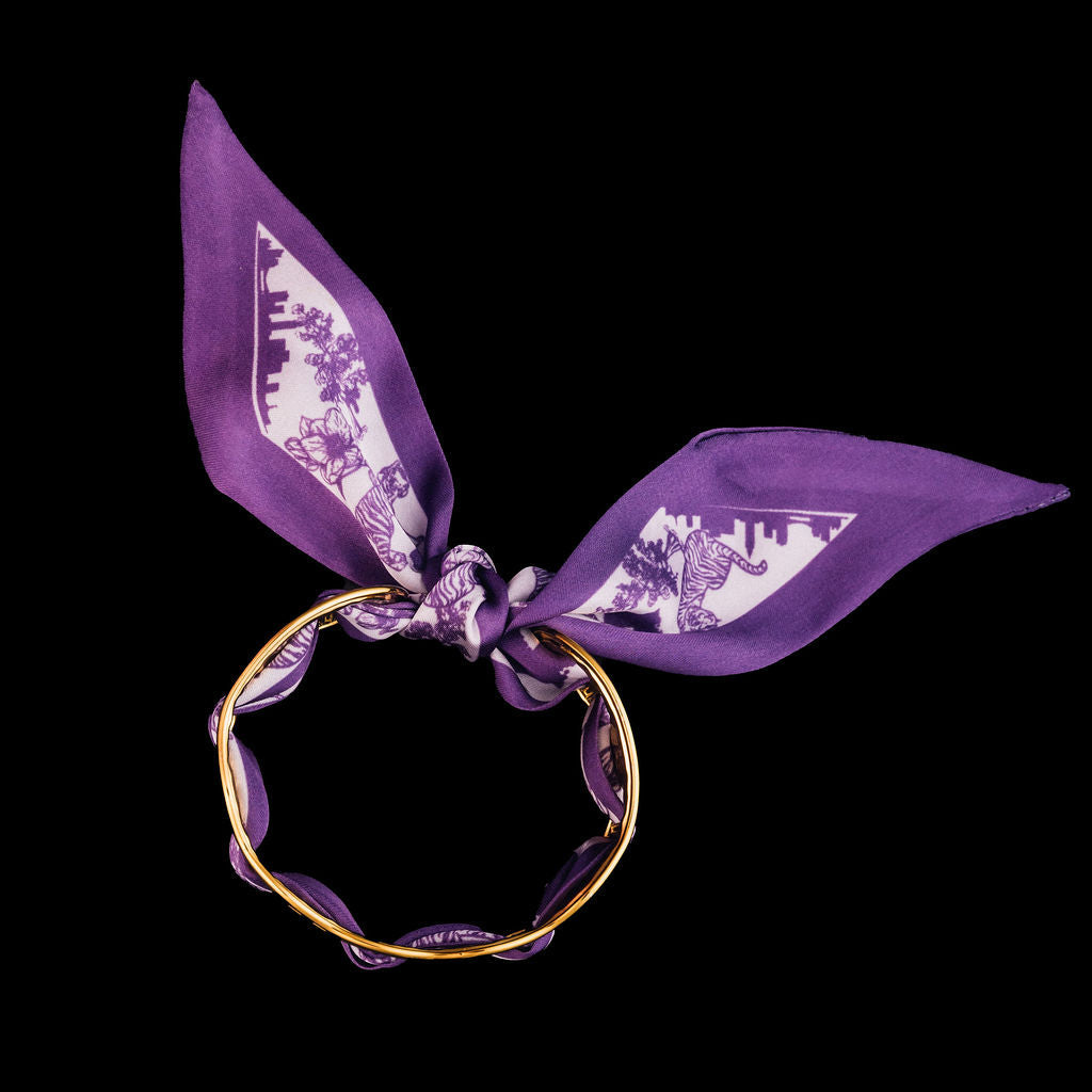 Gold cuff bracelets with purple scarf woven through it and tied in the back on a black background