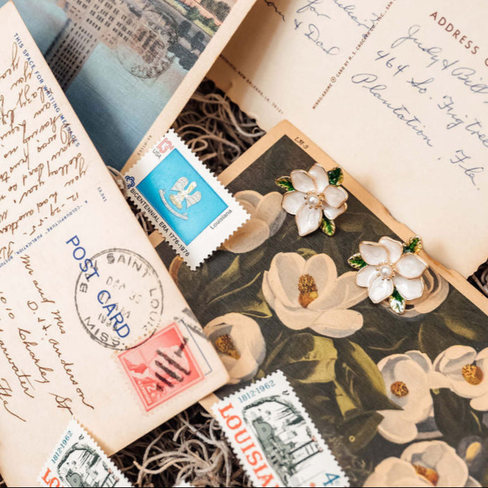 Collection of vintage postcards and stamps in a wooden box with magnolia stud earrings