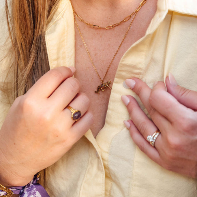 Close-up of a person wearing gold jewelry including a tiger necklace, ring, and bracelet.