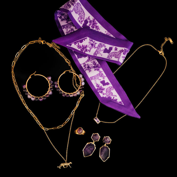 Purple scarf with tiger pattern, gold necklace, and earrings on a black background
